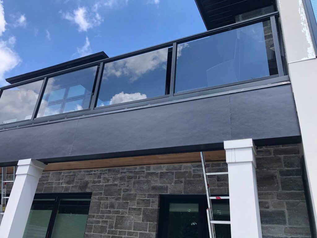 Balcony with glass railing and stone facade, with ladders indicating exterior renovation by Ideal Siding Memphis, TN