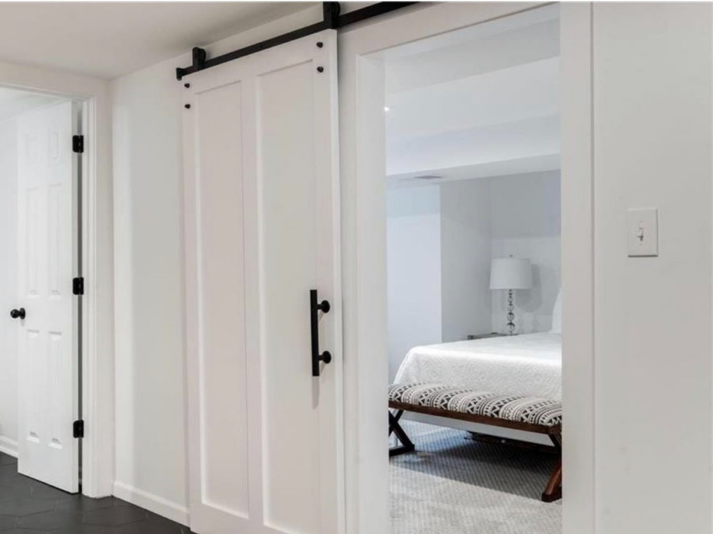 A stylish white barn door installed on a black track, leading into a renovated bedroom by Dogwood Renovation & Design, LLC in Kansas City, MO.