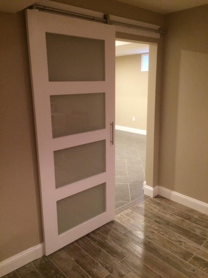 A modern white barn door with frosted glass panels installed on a track by Triple M Handyman in Portsmouth, NH.