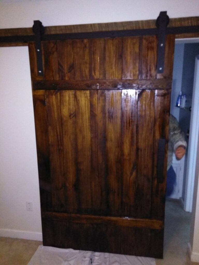 A newly installed wooden barn door with black hardware by Holy City Remodel in North Charleston, SC.