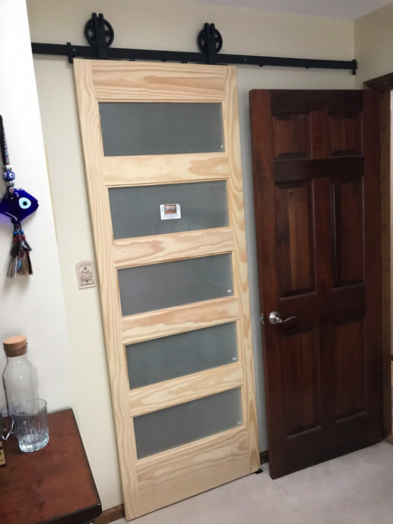 A new barn door ready for installation next to an existing door, a service provided by The Hot Handyman in Lawrence, KS.