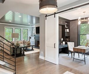 A modern white barn door installed by Zehnder Homes, Inc. connecting a living room and home office in Hamel, MN.
