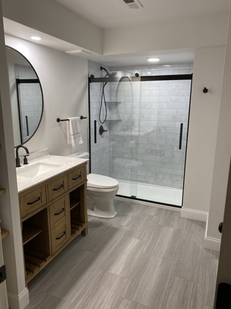 A renovated basement bathroom with a wood vanity, round mirror, and a walk-in shower by Westrick Homes in St. Louis, MO.