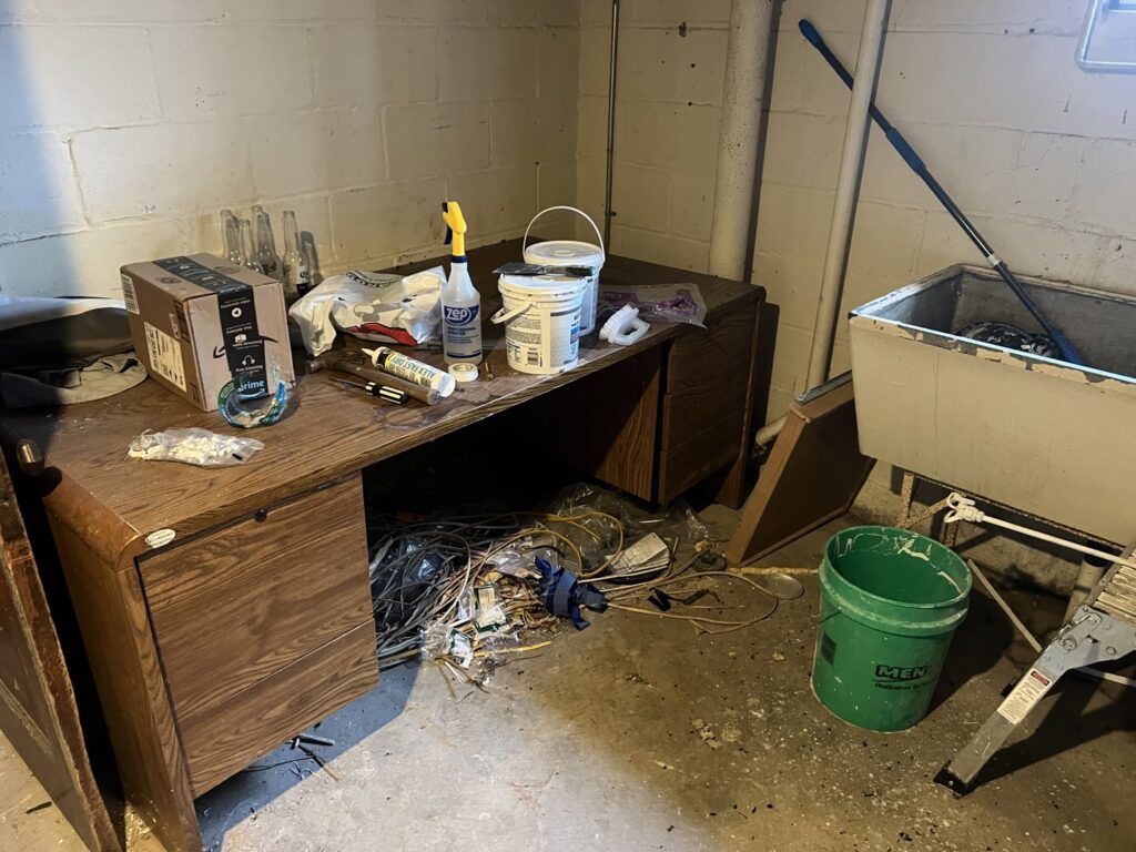 A cluttered basement area with an old desk, tools, and debris, requiring junk removal by Feelin Good Junk Removal & Estate Sales at 1111 Debra Lane.