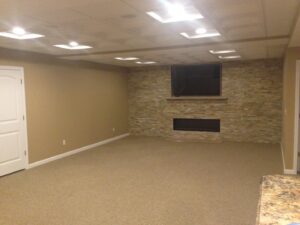 Finished basement living area with a stone fireplace and mounted TV by S. Brown Construction Co. in Lafayette, IN