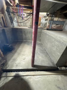 A concrete foundation or pit under construction in a basement, showing ongoing work by FH Perry Builder in Hopkinton, MA.
