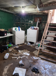 A cluttered basement laundry area with trash and debris on the floor, ready for junk removal by C&J junk removal llc in Akron, OH.