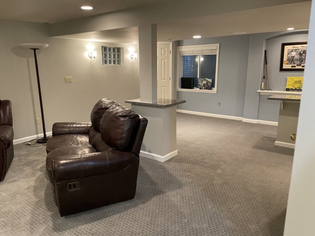 A renovated basement living area with new carpet and a staircase, showcasing work by RAW Renovation in Denver, CO.