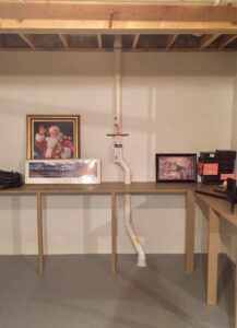 A vertical radon mitigation pipe installed through a workbench in an interior basement by All Ohio Radon Services in Akron, OH.