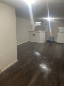 A renovated basement room with new dark laminate flooring and a white bar counter, completed by Knutson's Property Maintenance Llc in Williston, ND.