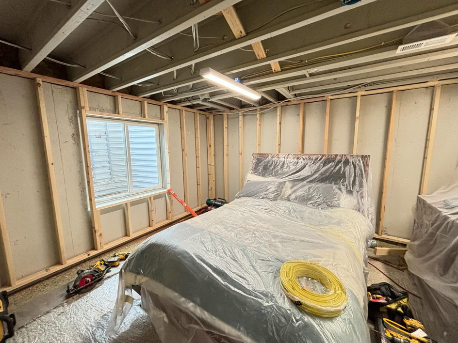 A basement renovation project showing wall framing, a covered bed, and tools by iFloor in Westminster, CO.