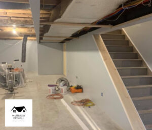 A basement under renovation with newly painted walls and a staircase, showing handyman work by Waterbury Drywall in Waterbury, CT.