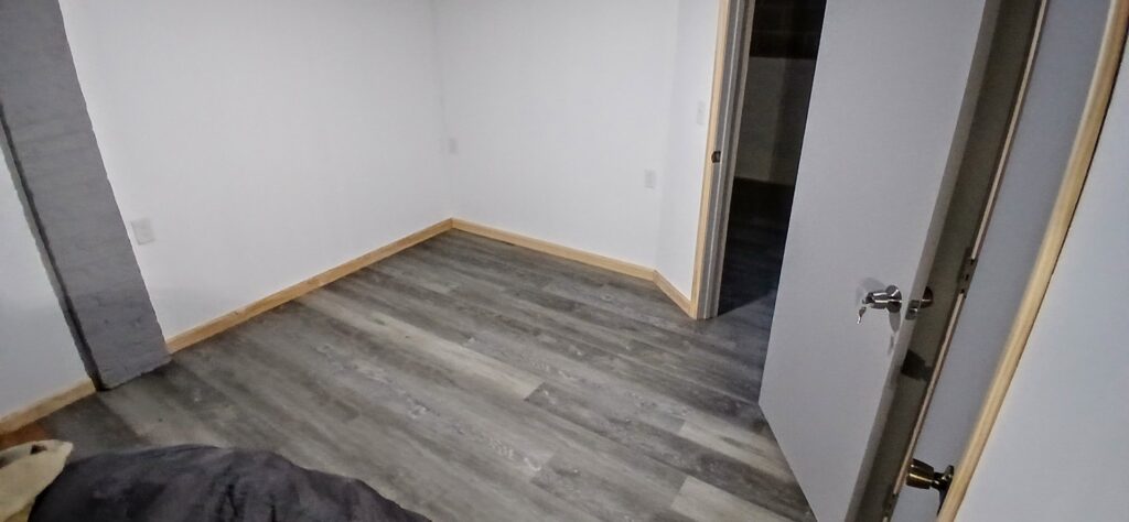 A newly renovated basement room with wood-look flooring and fresh paint by Prime Construction And Flooring in Lorain, OH.