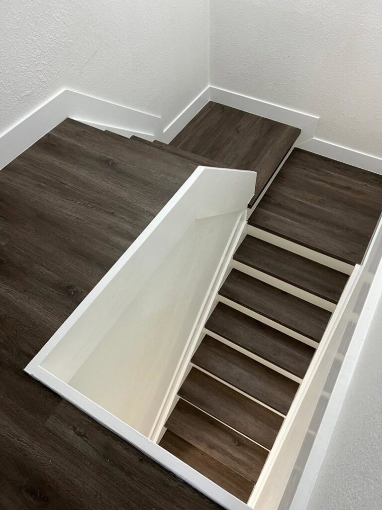 A view looking down into a basement staircase featuring dark wood-look flooring and white trim, installed by SD Masters in Miami, FL.