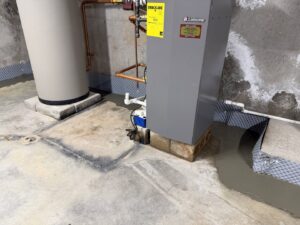 A basement area with a water heater and furnace, showing newly installed waterproofing membrane and drainage by B-Dry System of New England in North Billerica, MA.