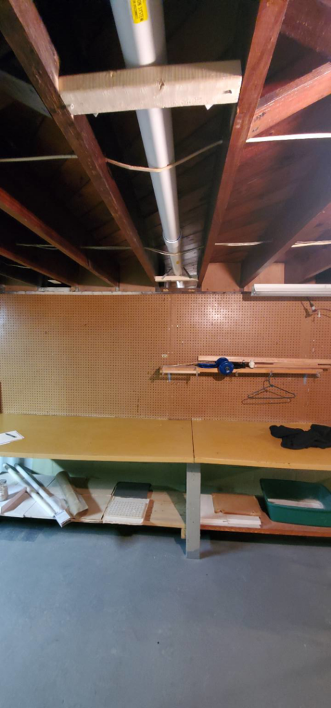 A basement workshop with radon mitigation piping installed in the exposed ceiling by All Ohio Radon Services in Akron, OH.