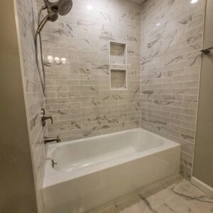 Bathroom with a bathtub and shower combo, featuring light grey marble-look subway tiles and two built-in niches by Supreme Tile & Flooring in Charlotte, NC.