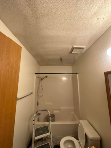 A bathroom with a step ladder and paint bucket, indicating a ceiling painting or repair job in progress by One Seven Painting LLC in Columbia, MO.