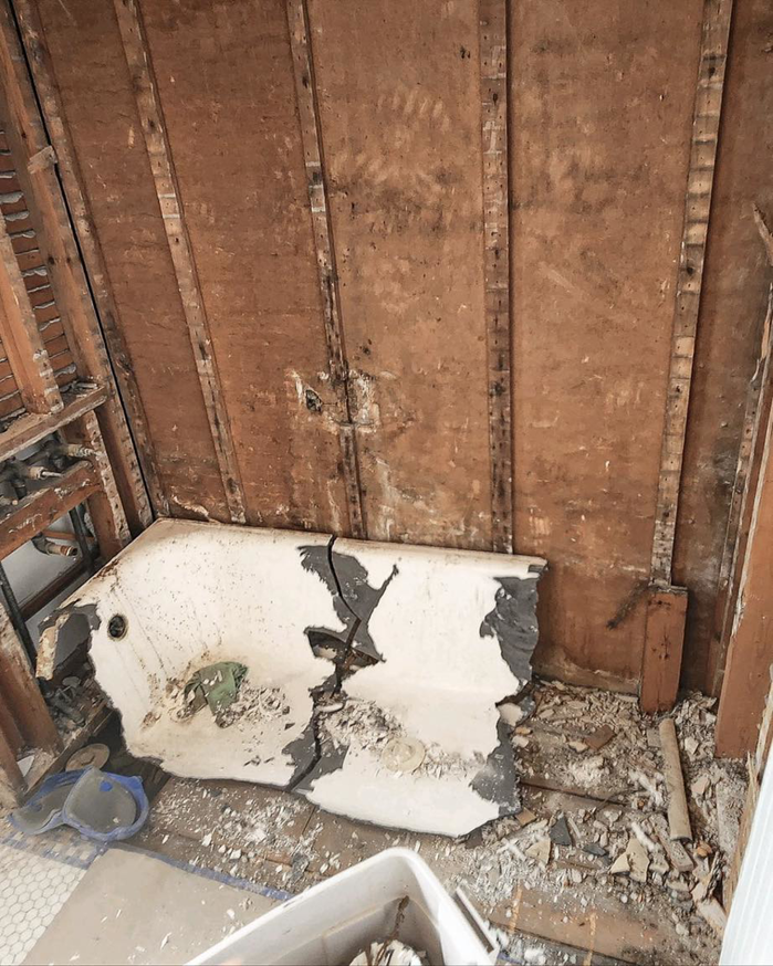 A bathroom undergoing demolition with a broken bathtub and exposed walls, handled by Brian's Tiles in Duluth, MN.