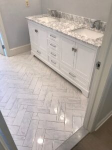 A bathroom featuring a new double vanity and herringbone pattern floor tile by Prenga Remodeling in Orange, CT