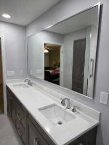 A newly installed bathroom double vanity with white countertops and a large mirror by Creative Building & Remodeling in Warren, MI