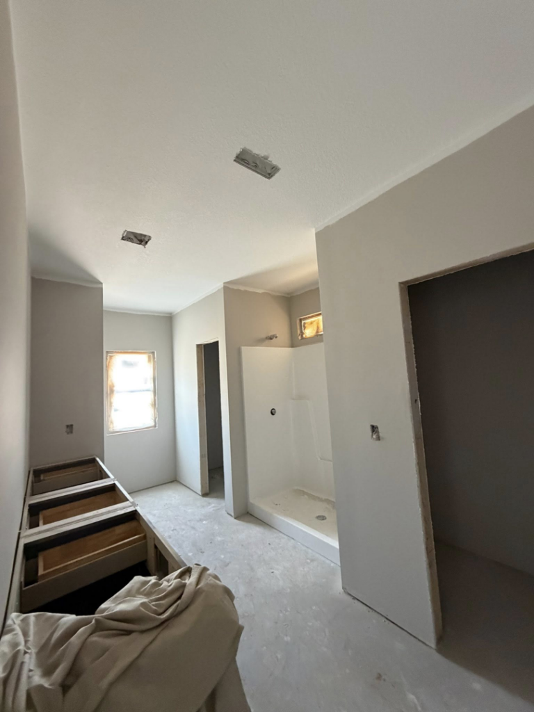 A bathroom under renovation with new drywall, cabinet bases, and a shower stall installed by JM Drywall LLC in Dothan, AL.