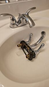 A bathroom sink faucet being replaced, with the old faucet in the sink, by Medina's Handyman LLC in Las Vegas, NV