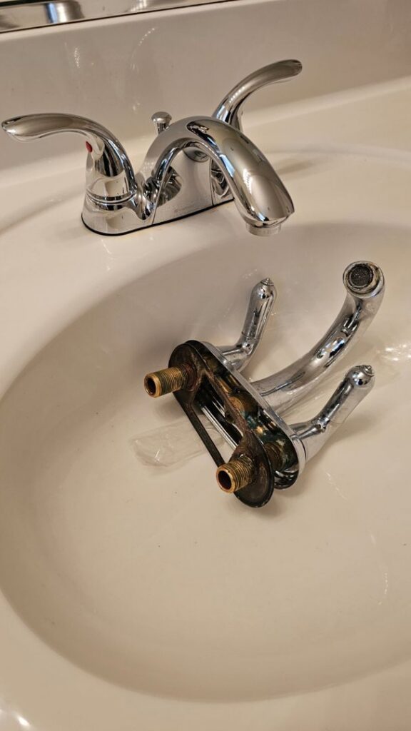 A bathroom sink faucet being replaced, with the old faucet in the sink, by Medina's Handyman LLC in Las Vegas, NV