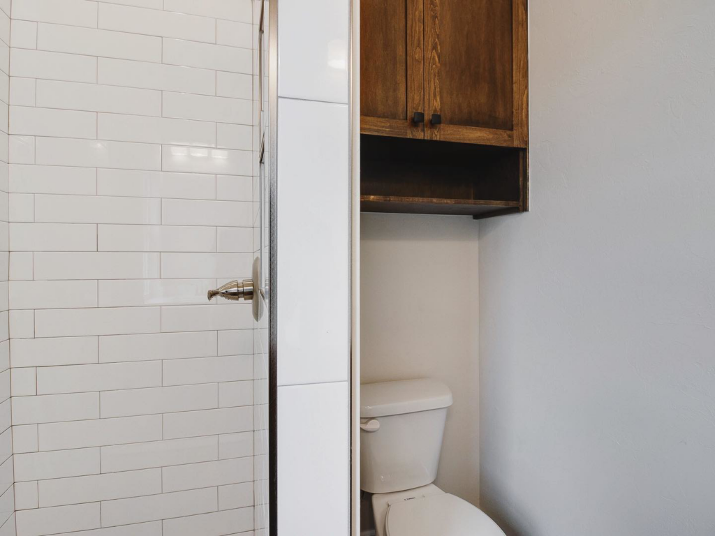 A modern bathroom with a toilet, shower, and wooden cabinet installed by Power Roofing & Construction in Norman, OK.
