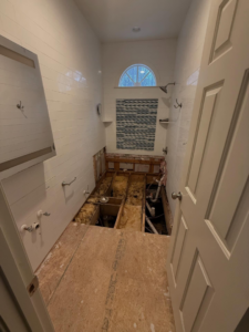 A bathroom undergoing renovation with the floor removed, exposing joists and plumbing, by Rice Building Company in Rocky Mount, NC.