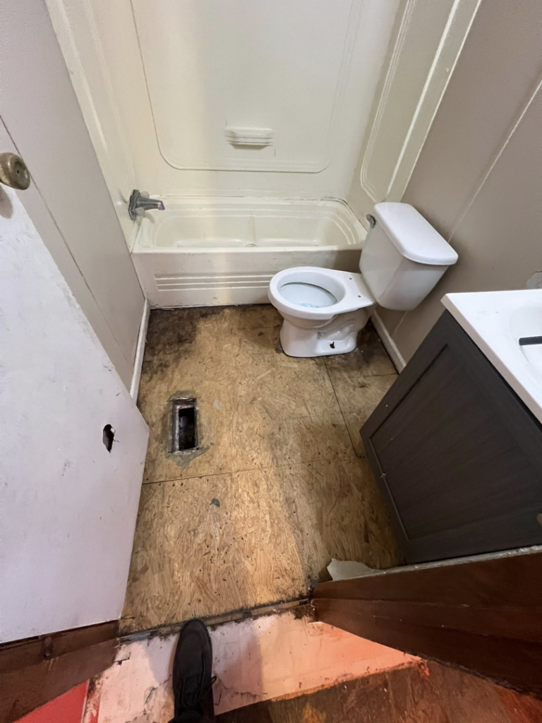 A bathroom with the floor removed down to the subfloor, showing a toilet and bathtub, ready for renovation by Cosa Cleanouts & Junk Removal in Topeka, KS.