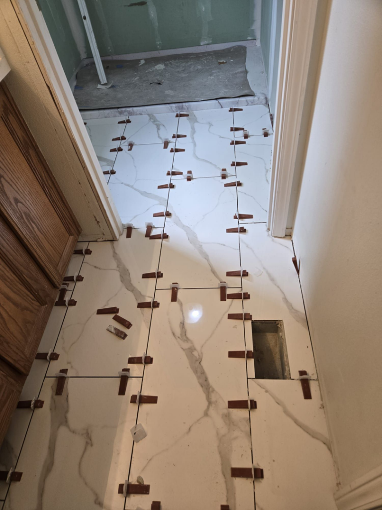 Installing new white marble-look floor tiles in a bathroom, using spacers, by Fullhouse Builders LLC in Gig Harbor, WA