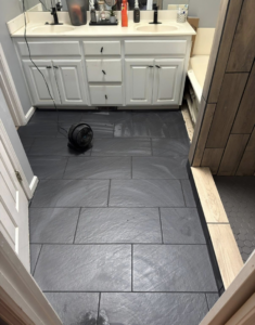 Newly installed dark grey tile flooring in a bathroom with a double vanity by Jason Roberts Painting and Remodeling in Louisville, KY.