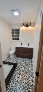 A renovated bathroom with patterned floor tiles and a dark wood vanity with black faucets by M J Services Home Remodeling in Gaithersburg, MD.