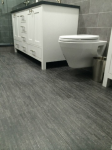 Textured grey floor tiles, a white vanity, and a wall-mounted toilet in a renovated bathroom by Executech Interiors in Yonkers, NY