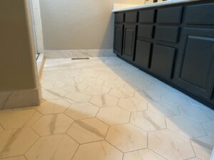 A newly installed bathroom floor with white hexagonal tiles and a dark vanity, by Handyman Connection of Fort Collins in Fort Collins, CO