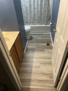 A renovated bathroom with new wood-look tile flooring, toilet, and vanity, completed by Newhouse Construction St Louis in St. Louis, MO.