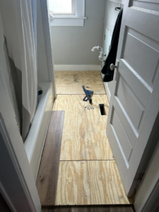 A bathroom showing flooring installation in progress with subfloor and a new plank, by CJ Flooring LLC in Flat Rock, MI.