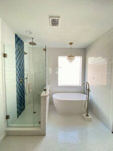 A renovated bathroom with a freestanding tub and a walk-in shower featuring blue accent tiles, completed by Whole House Remodel & Design North Dallas Tx in Frisco, TX.