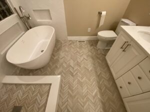 A renovated bathroom featuring herringbone pattern floor tiles and a white vanity by Goubar Tile And More in Raleigh, NC.