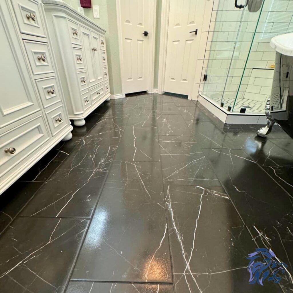 A renovated bathroom showcasing elegant black marble-look tile flooring and white vanities, by Roaring Lion Renovations, LLC in Houston, TX.