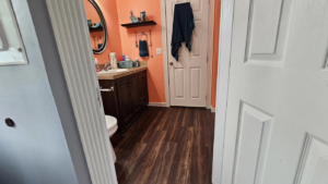A bathroom with old dark wood-look flooring before renovation by Goulds Family Property Management and Handyman Services in Searsport, ME.