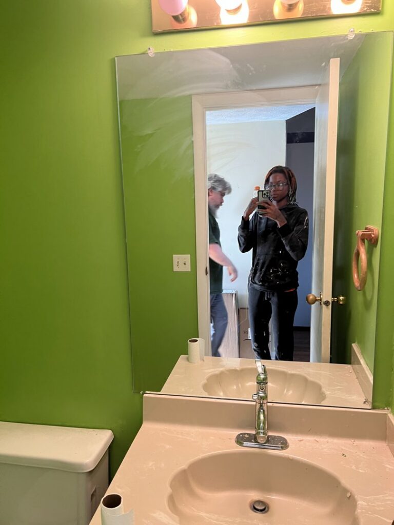 A bathroom with green painted walls, a mirror, and a sink, showing recent painting work by JW Contracting Services, LLC in Dayton, OH.