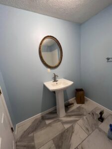 A newly installed pedestal sink, mirror, and tile flooring in a bathroom by The Golden Touch handyman services in Huntington, WV.