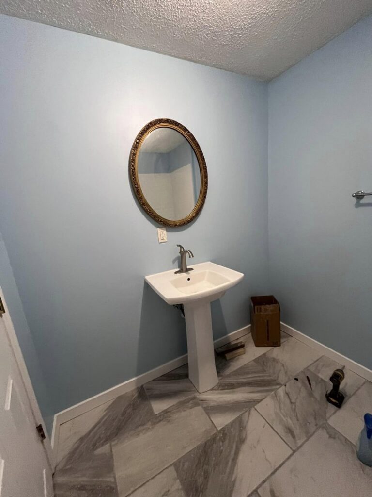 A newly installed pedestal sink, mirror, and tile flooring in a bathroom by The Golden Touch handyman services in Huntington, WV.