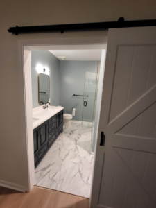 A newly remodeled bathroom with a barn door, double vanity, and glass shower by Nance Brothers, LLC in Matthews, NC.