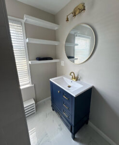 A renovated bathroom featuring a blue vanity, gold fixtures, and floating shelves by Garrett Group Construction in Philadelphia, PA.