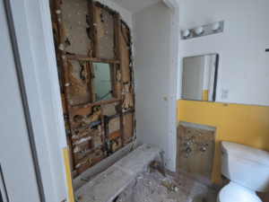 A bathroom during a remodel, showing wall demolition, exposed studs, insulation, and plumbing work by Joel's Handyman in Ogden, UT.