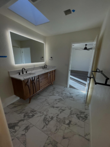 A completed bathroom remodel with a stylish double vanity and illuminated mirror by Raven Construction LLC in Tucson, AZ.