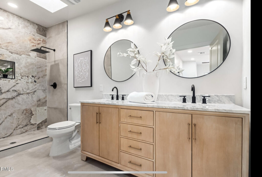 A newly remodeled bathroom featuring a double vanity, round mirrors, and a walk-in shower with marble-look tiles by American Wolf Construction in Mesa, AZ